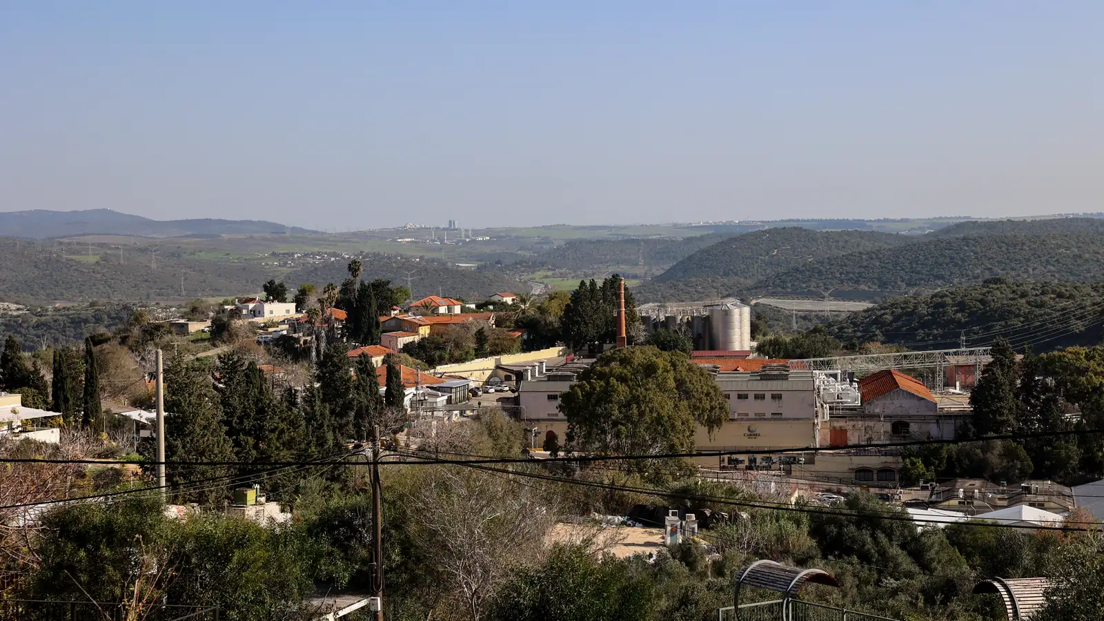 נוף פתוח של עמק ובתי מושבה בין עצים, נשקף מהמתחם