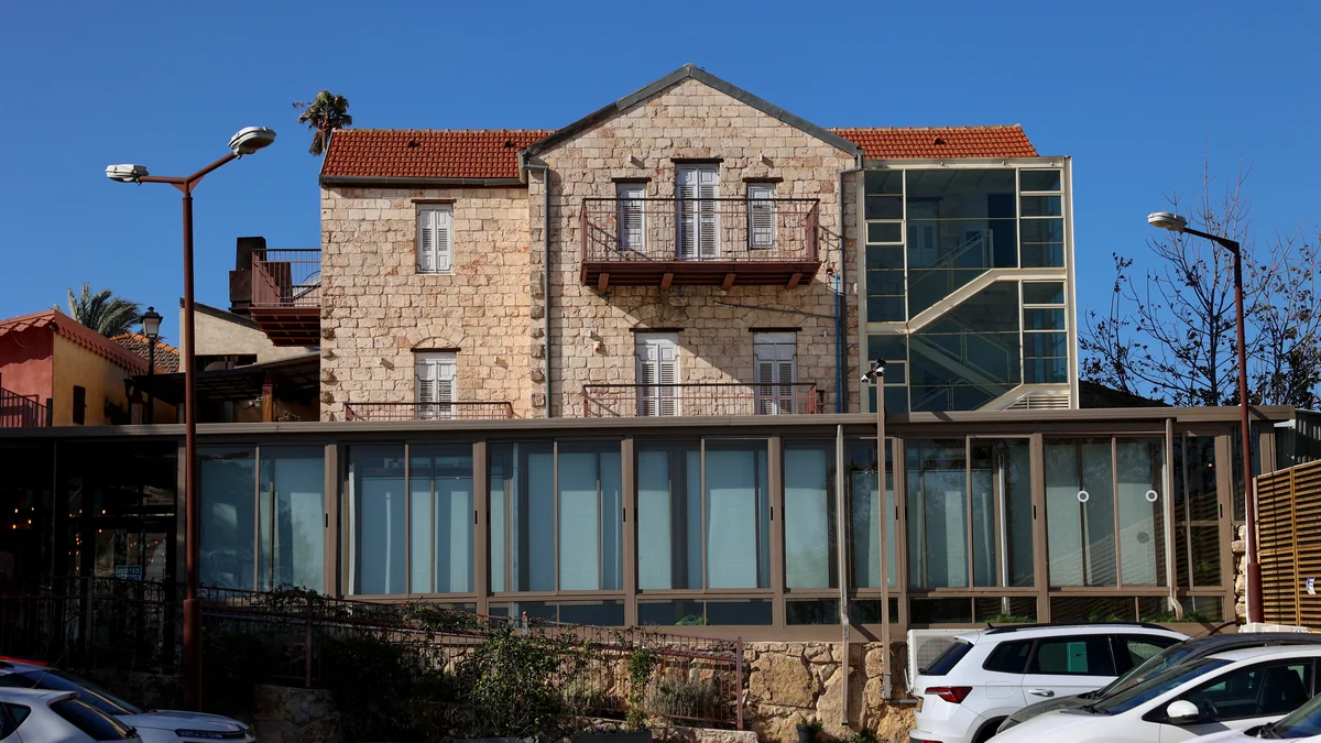 חזית המתחם מבנה אבן היסטורי דו קומתי עם חזית זכוכית וחניון לפניו